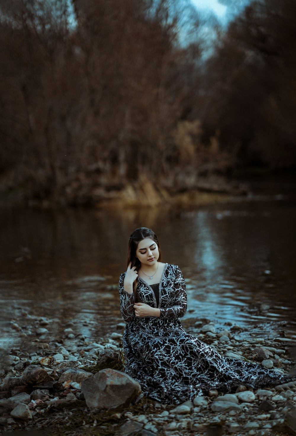 a woman in a dress sitting on rocks near a river