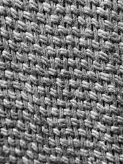 A close-up view of a woven textile, highlighting the texture and pattern of interlaced fibers. The image showcases the intricate details of the weave, emphasizing the individual strands and the way they are intertwined.