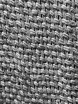 A close-up view of a woven textile, highlighting the texture and pattern of interlaced fibers. The image showcases the intricate details of the weave, emphasizing the individual strands and the way they are intertwined.