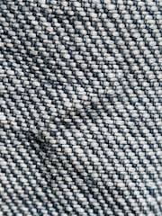 Close-up view of a woven textile pattern, featuring tightly interlaced threads that create a textured surface. The material displays a diagonal weave with contrasting colors of dark blue and light beige.