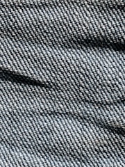 A close-up view of denim fabric with visible texture, showing the intricate weave pattern and shades of blue and white threads.