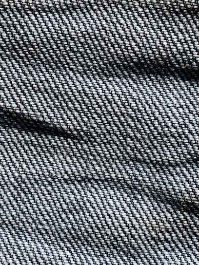 A close-up view of denim fabric with visible texture, showing the intricate weave pattern and shades of blue and white threads.