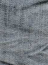 A close-up view of denim fabric with visible blue and white threads intersecting to form a classic twill pattern.