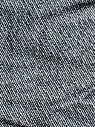 A close-up view of denim fabric with visible blue and white threads intersecting to form a classic twill pattern.