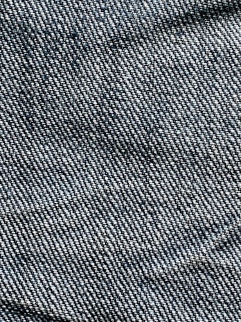 A close-up view of denim fabric with visible blue and white threads intersecting to form a classic twill pattern.