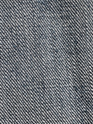 A close-up view of a textured fabric with a woven pattern. The fibers alternate between dark blue and white threads, creating a characteristic denim appearance.