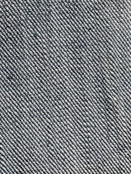 A close-up view of a woven fabric texture featuring a dense pattern of interlaced threads. The fabric appears sturdy and thick, with a prominent diagonal weave pattern, indicative of denim material.