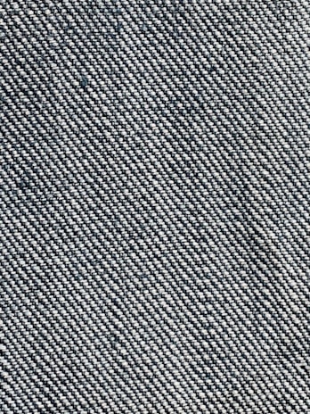 A close-up view of a woven fabric texture featuring a dense pattern of interlaced threads. The fabric appears sturdy and thick, with a prominent diagonal weave pattern, indicative of denim material.