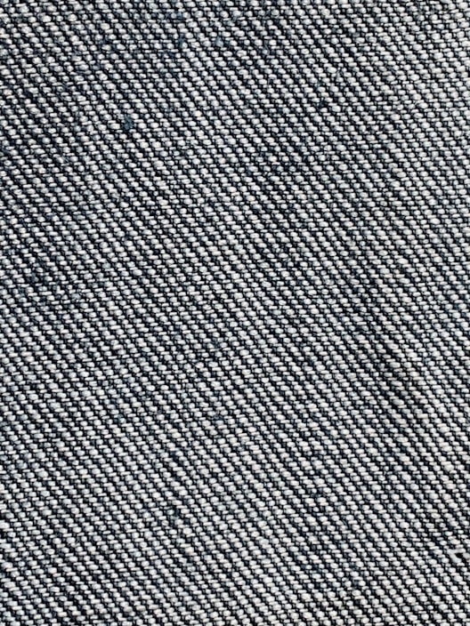 A close-up view of a woven fabric texture featuring a dense pattern of interlaced threads. The fabric appears sturdy and thick, with a prominent diagonal weave pattern, indicative of denim material.