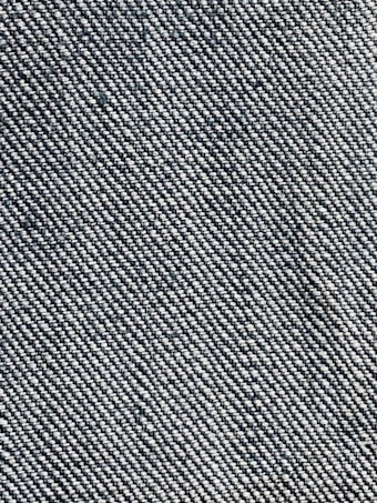 A close-up view of a woven fabric texture featuring a dense pattern of interlaced threads. The fabric appears sturdy and thick, with a prominent diagonal weave pattern, indicative of denim material.