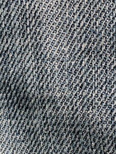 A close-up view of textured denim fabric with a detailed, diagonal weave pattern in shades of blue and white.