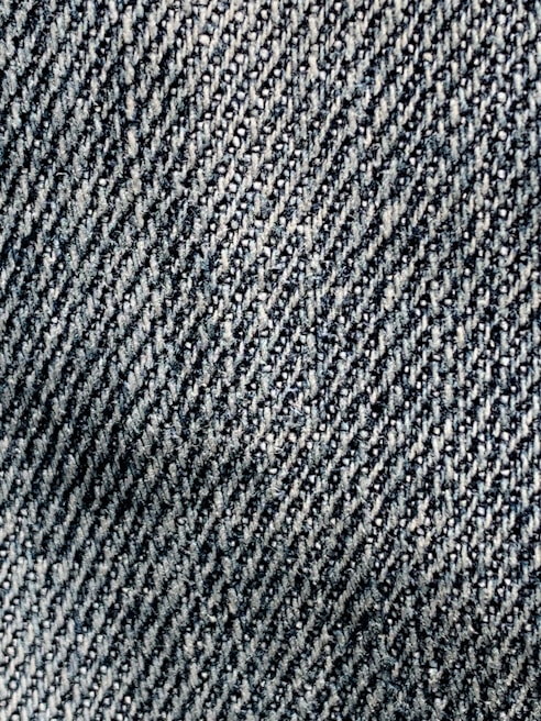 A close-up view of textured denim fabric with a detailed, diagonal weave pattern in shades of blue and white.