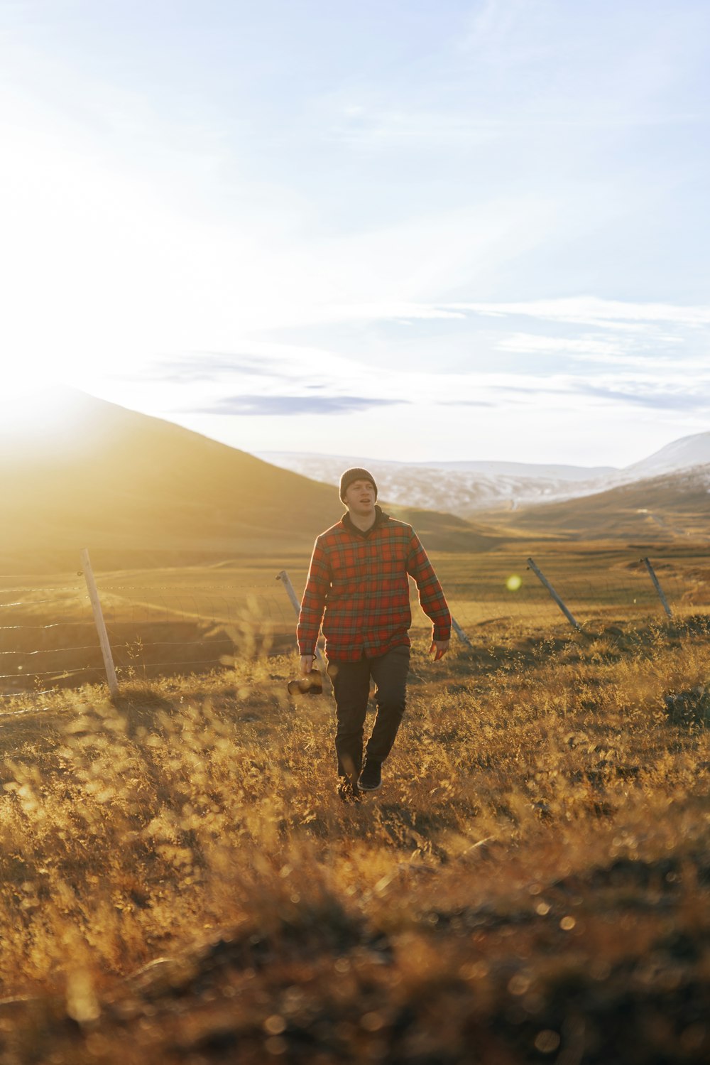 a man is walking through a field with mountains in the background