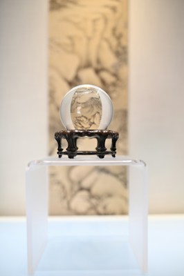 A crystal ball is placed on an ornate stand. The background features a blurred artistic depiction that resembles traditional ink wash painting. The setup is minimalist, focused on the elegant presentation of the crystal ball on a transparent surface.