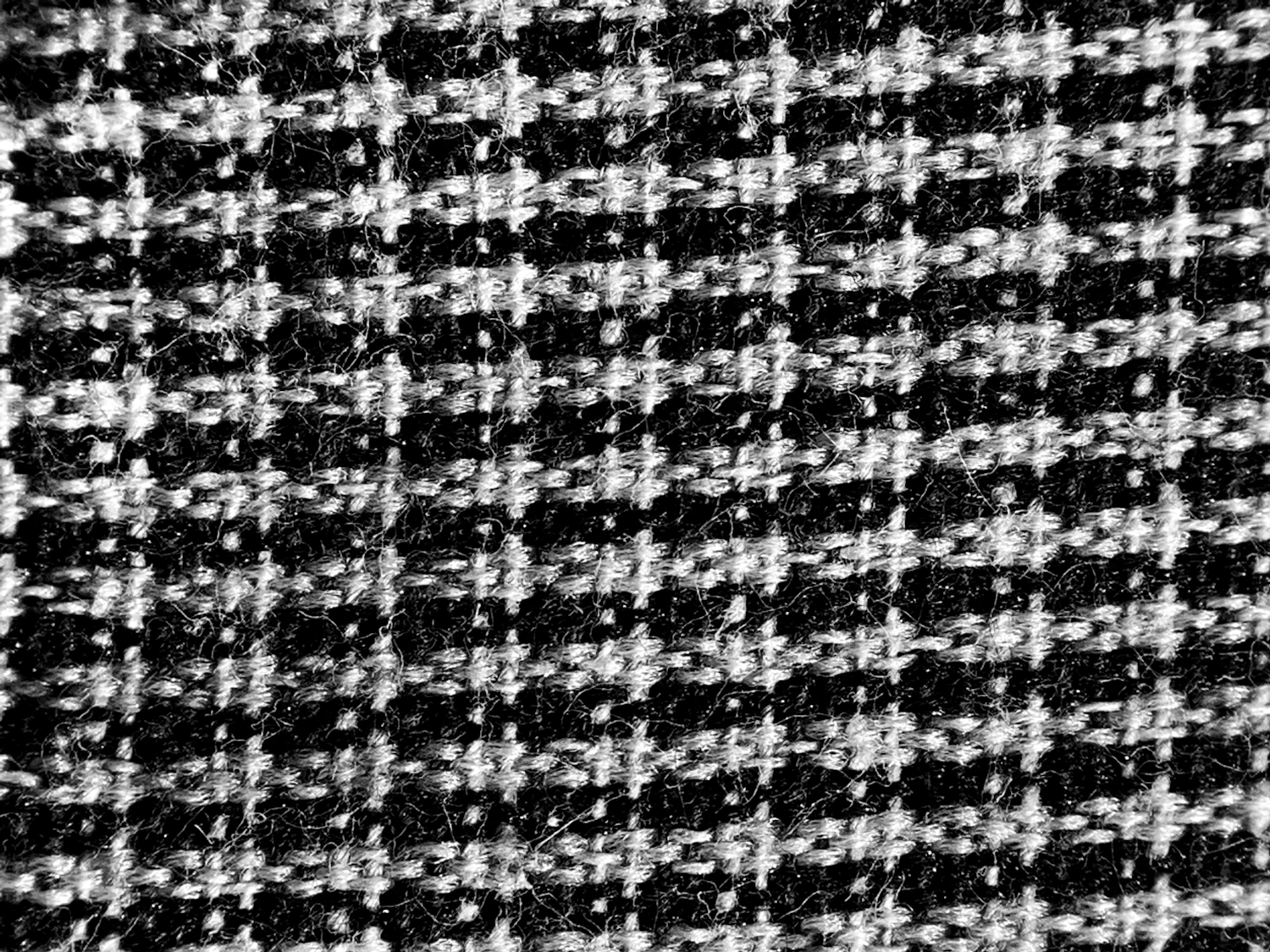 A square of black and chalk houndstooth coating lying open on the cutting table