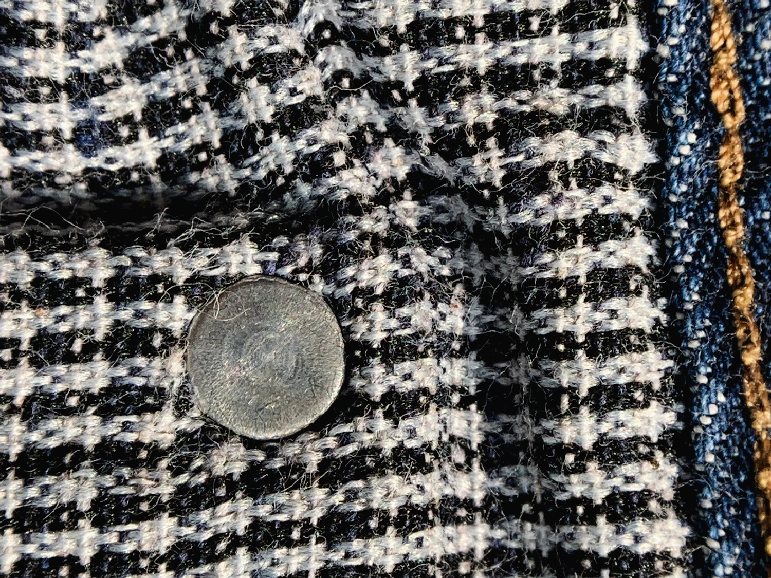 Navy and oat Cheviot check tweed with a horn button resting on the weave