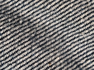 A close-up view of a woven fabric with a diagonal black and white striped pattern. The texture shows the interlacing fibers and slight variations in color and thickness, creating a tactile, three-dimensional appearance.
