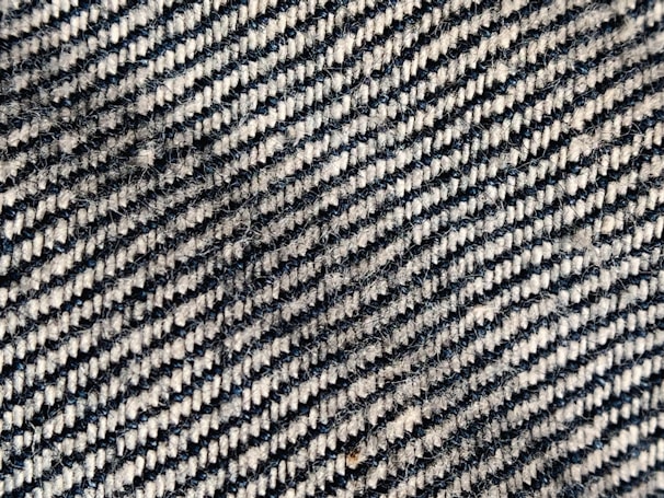 A close-up view of a woven fabric with a diagonal black and white striped pattern. The texture shows the interlacing fibers and slight variations in color and thickness, creating a tactile, three-dimensional appearance.