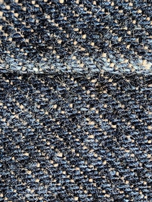 Close-up of a textured beige fabric with subtle black and blue threads woven in.