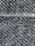 A close-up view of a textured fabric with interwoven dark blue and beige threads, creating a detailed woven pattern. The fibers appear slightly fuzzy, indicating a tightly woven, rough textile.