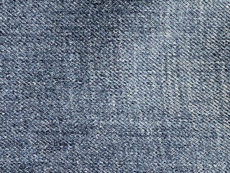 A close-up of blue denim fabric showing a detailed weave pattern with variations in shading and texture.