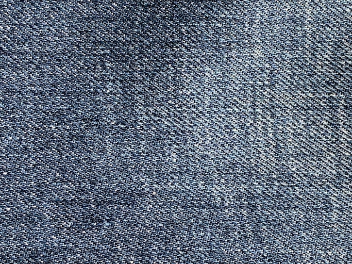 A close-up of blue denim fabric showing a detailed weave pattern with variations in shading and texture.