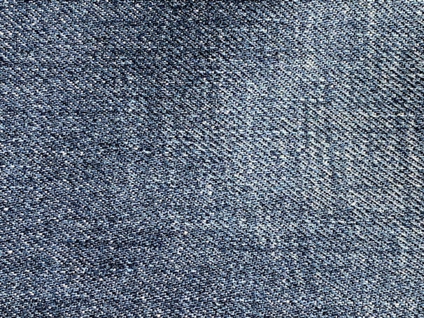 A close-up of blue denim fabric showing a detailed weave pattern with variations in shading and texture.