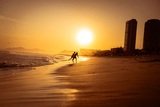 A serene beach with golden sand, turquoise water, and a couple walking hand in hand during sunset.