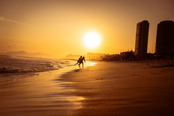 A serene beach with golden sand, turquoise water, and a couple walking hand in hand during sunset.