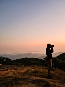 Cinematic shot of a travel influencer capturing a sunrise over a mountain range.