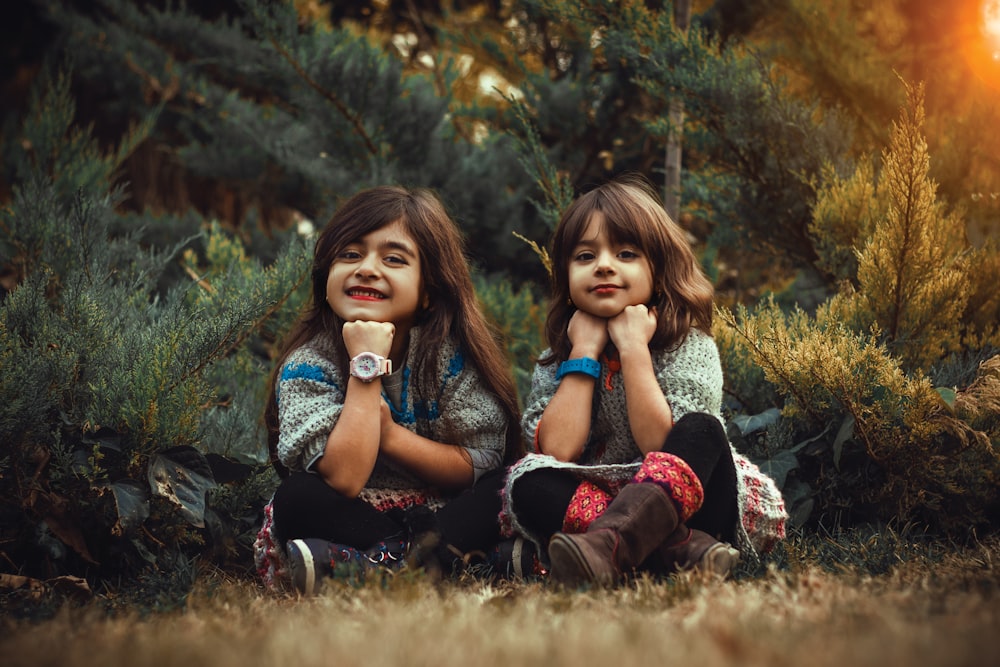 two young girls sitting on the ground in front of trees