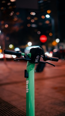 Close-up of hands gripping scooter handlebars with lime green accents, city lights blurred in the background.