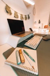 a desk with a laptop, keyboard, and notebook on it