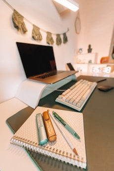 a desk with a laptop, keyboard, and notebook on it