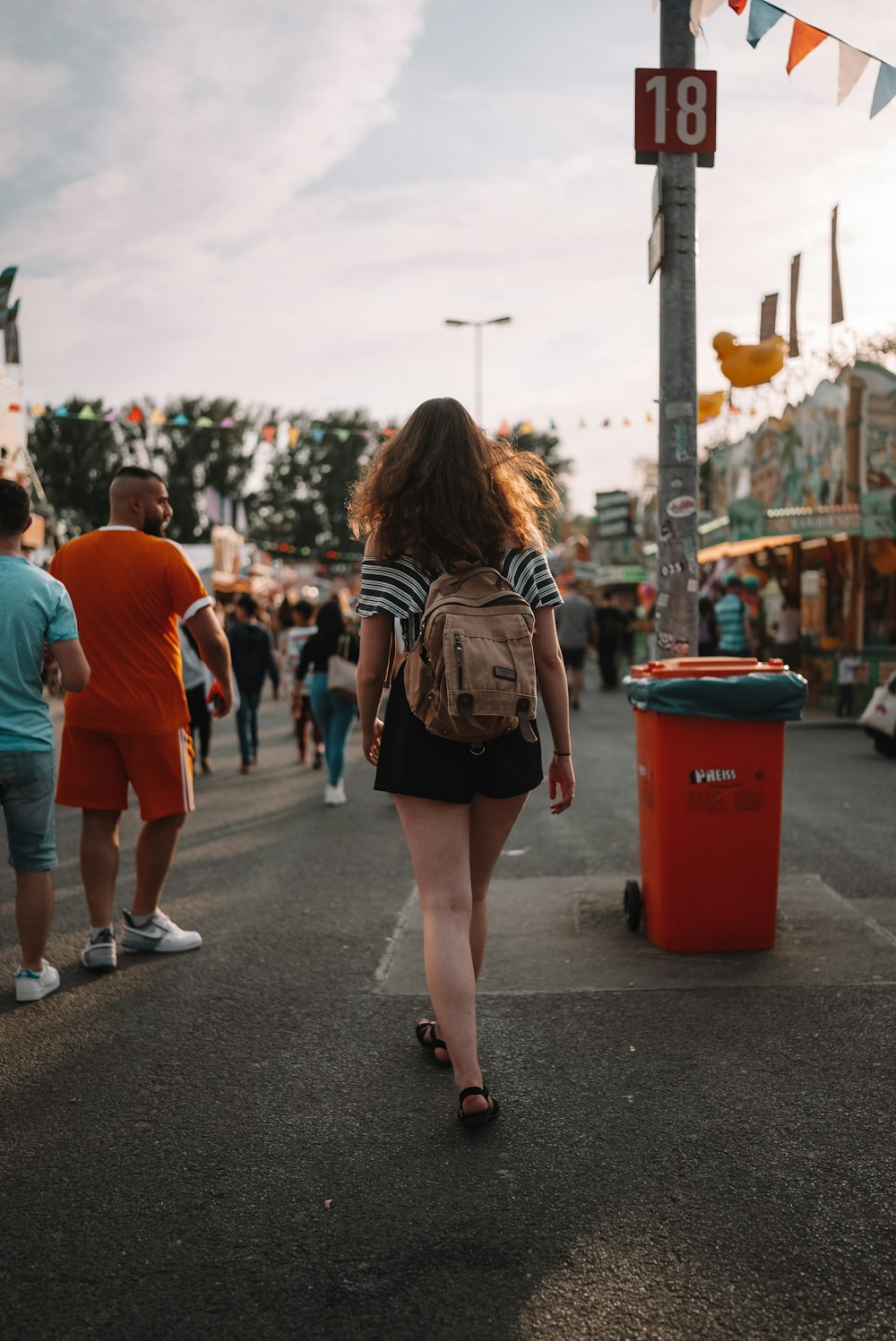 a woman walking down a street next to a red trash can
