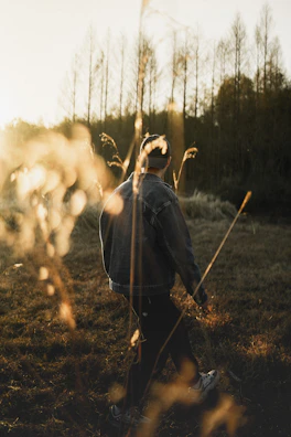 A woman in a classic chambray shirt and jeans walking through a field of tall grass at golden hour.