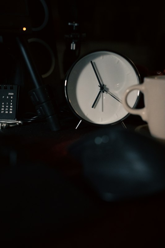 A white desk clock beside a coffee mug and a small desk calendar