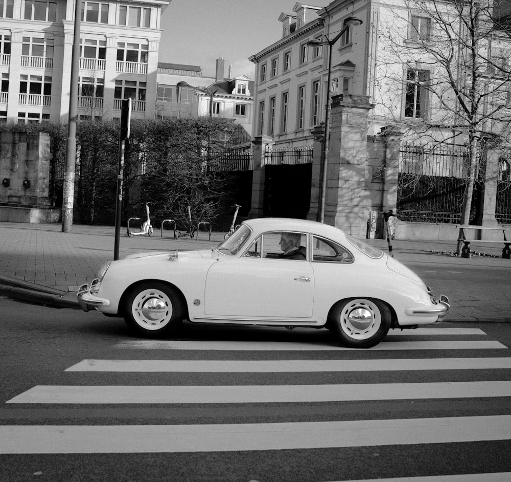 a white car driving down a street next to tall buildings