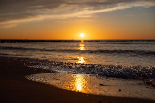 A serene sandy beach at sunset with gentle waves under a blue sky, reflecting the calming blue and gold theme.