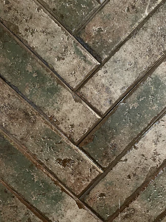 Rustic wooden-look tiles arranged in a herringbone pattern on a floor.