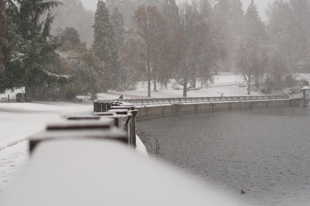 a snow covered park with benches and a lake