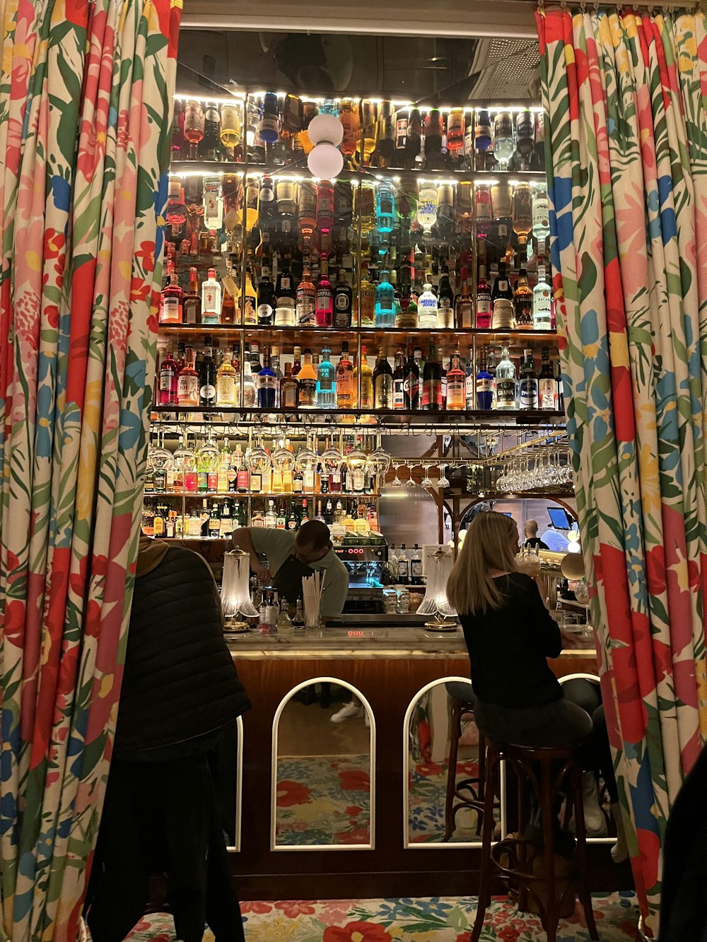two people sitting at a bar with a lot of bottles behind them