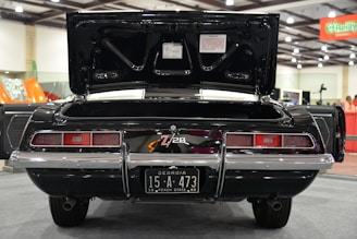 A classic black car with an open trunk is displayed indoors. The car has a license plate from Georgia, marked 15-A-473, 1969 Peach State. The vehicle features dual exhausts and a distinctive rear tail light design. The exhibition hall is well-lit with visible signage and other vehicles in the background.