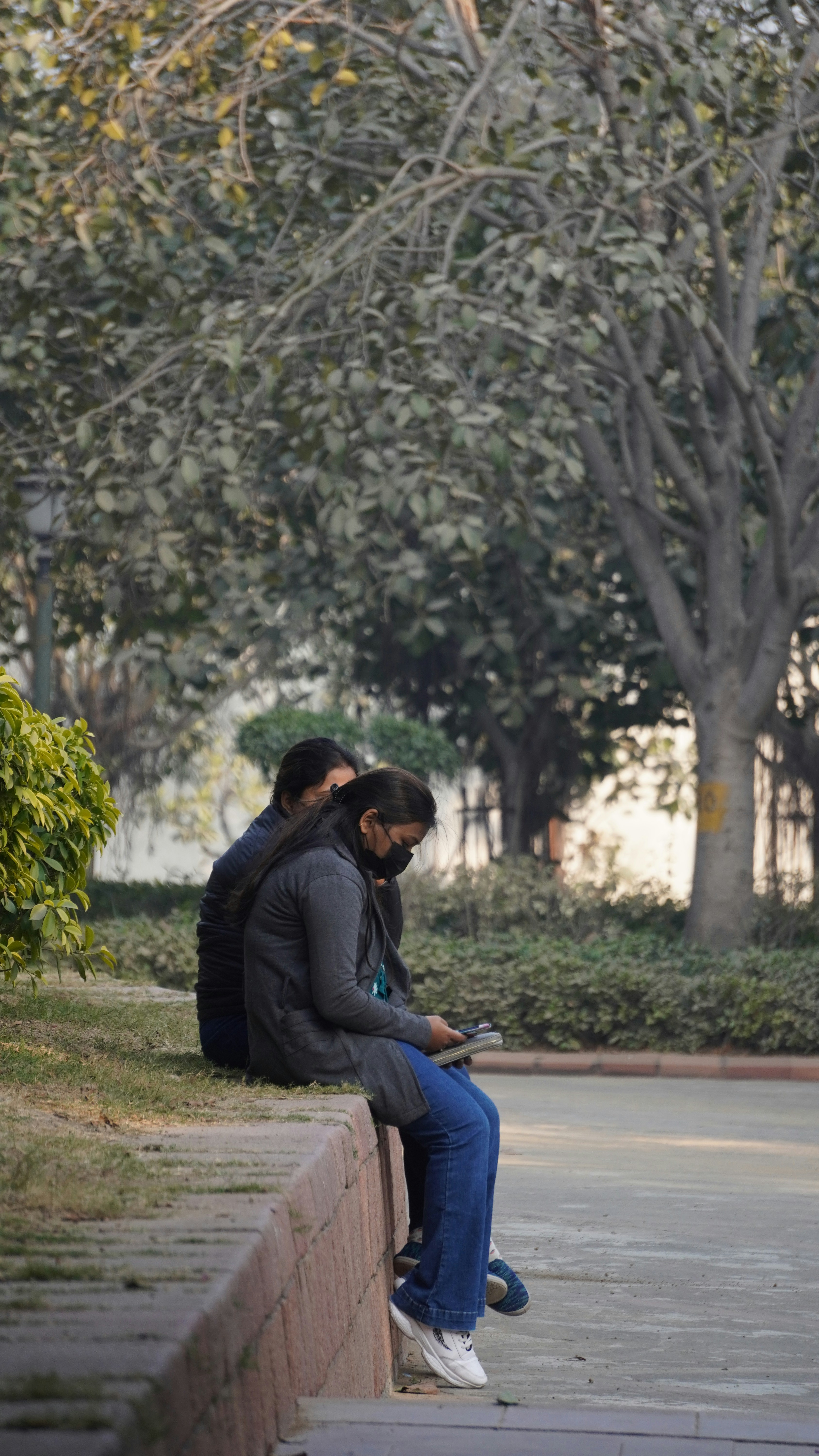two people sitting on a wall looking at their cell phones