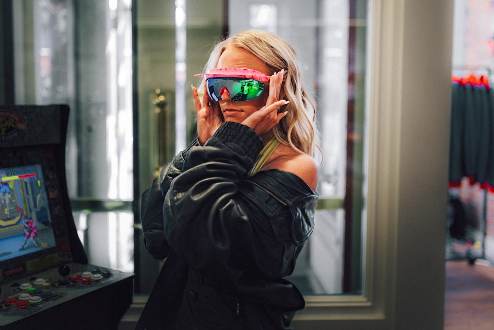 a woman in a black jacket is holding up a pair of sunglasses