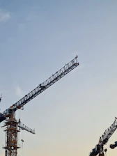 Engineers reviewing blueprints on a construction site with cranes and buildings in the background under soft morning light.
