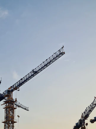 Cranes lifting heavy materials against a clear blue sky during early morning work.