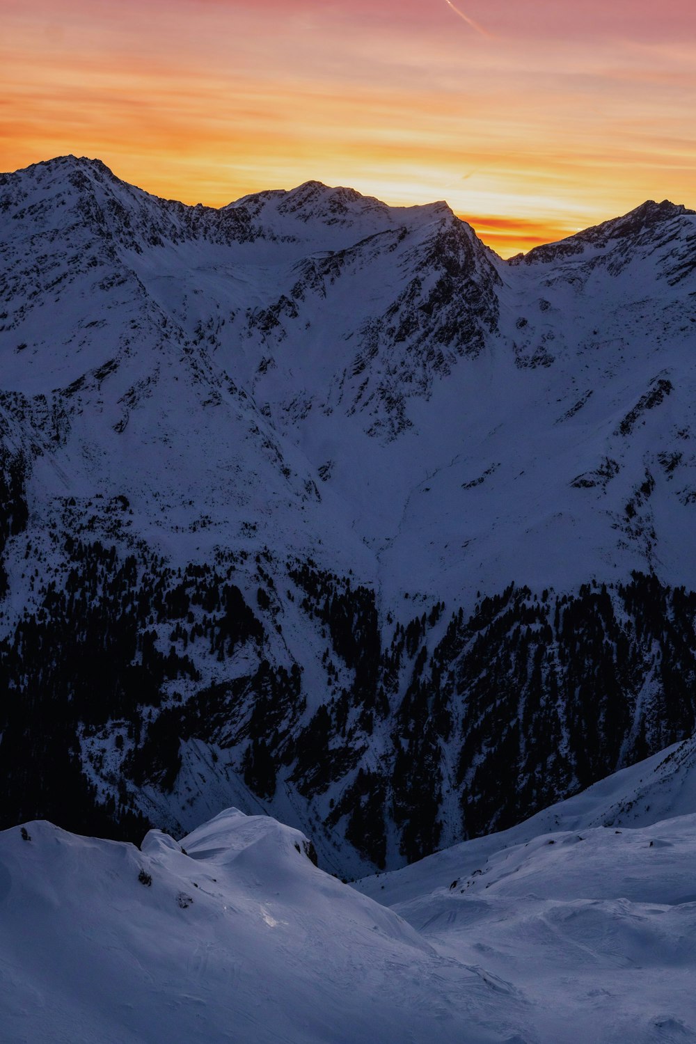 the sun is setting over a snowy mountain range