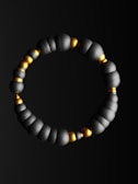 A bracelet composed of alternating matte black and shiny gold spherical beads arranged in a continuous circular pattern. The black beads have a matte finish while the gold beads are smaller and metallic.