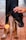 A black and tan dog stands on a tiled surface with its head lowered. One hand gently pats the dog's head while another hand offers a round biscuit.
